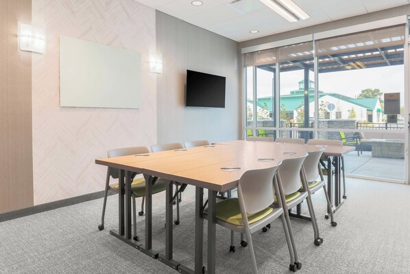 A conference room with a large table, chairs, a flat-screen TV, and a view of an outdoor area with a building and greenery. - SpringHill Suites by Marriott Tallahassee North (Tallahassee)