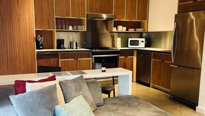 Eine moderne Küche mit Holdekor-Schränken, Edelstahlgeräten und einem grauen Ecksofa mit Kissen.