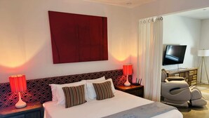 Ein Hotelzimmer mit einem großen Bett, zwei Nachttischen mit Lampen, einem Fernseher, einem Massagesessel und einem roten abstrakten Gemälde an der Wand.