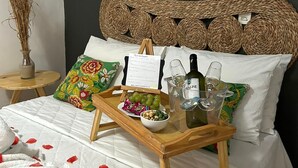 Una cama bien hecha con una bandeja de madera que contiene una botella, vasos y aperitivos.