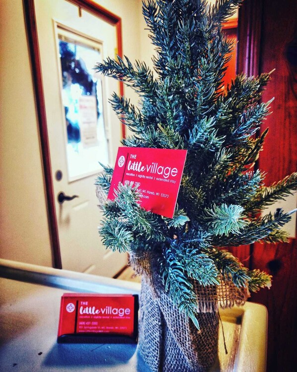 A small Christmas tree with a red sign labeled "The Little Village" in a room with a wooden door and a framed picture on the wall. - King Bedroom Suite at The Little Village (Mount Horeb)