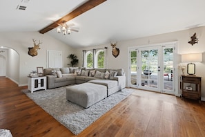 A spacious living room with a sectional sofa, a fireplace, and a view through glass doors.