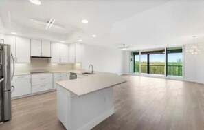 Una cocina moderna con una isla grande, muebles blancos y vistas a un paisaje verde a través de amplios ventanales.