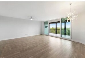 A spacious room with a large sliding glass door leading to a balcony, a ceiling fan, and a modern chandelier. - Paradise in Naples (Naples)