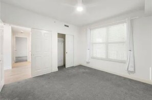 A room with a grey carpet, white walls, a large window with blinds, and a door leading to another room. - Paradise in Naples (Naples)
