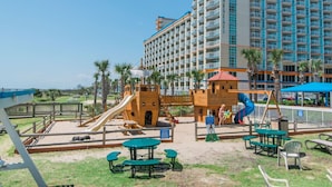 A playground with slides and climbing structures, surrounded by palm trees and a large hotel building in the background. - 3 bedroom 2 Bath, Unit 521, Unobstructed Ocean View, water park (Myrtle Beach)
