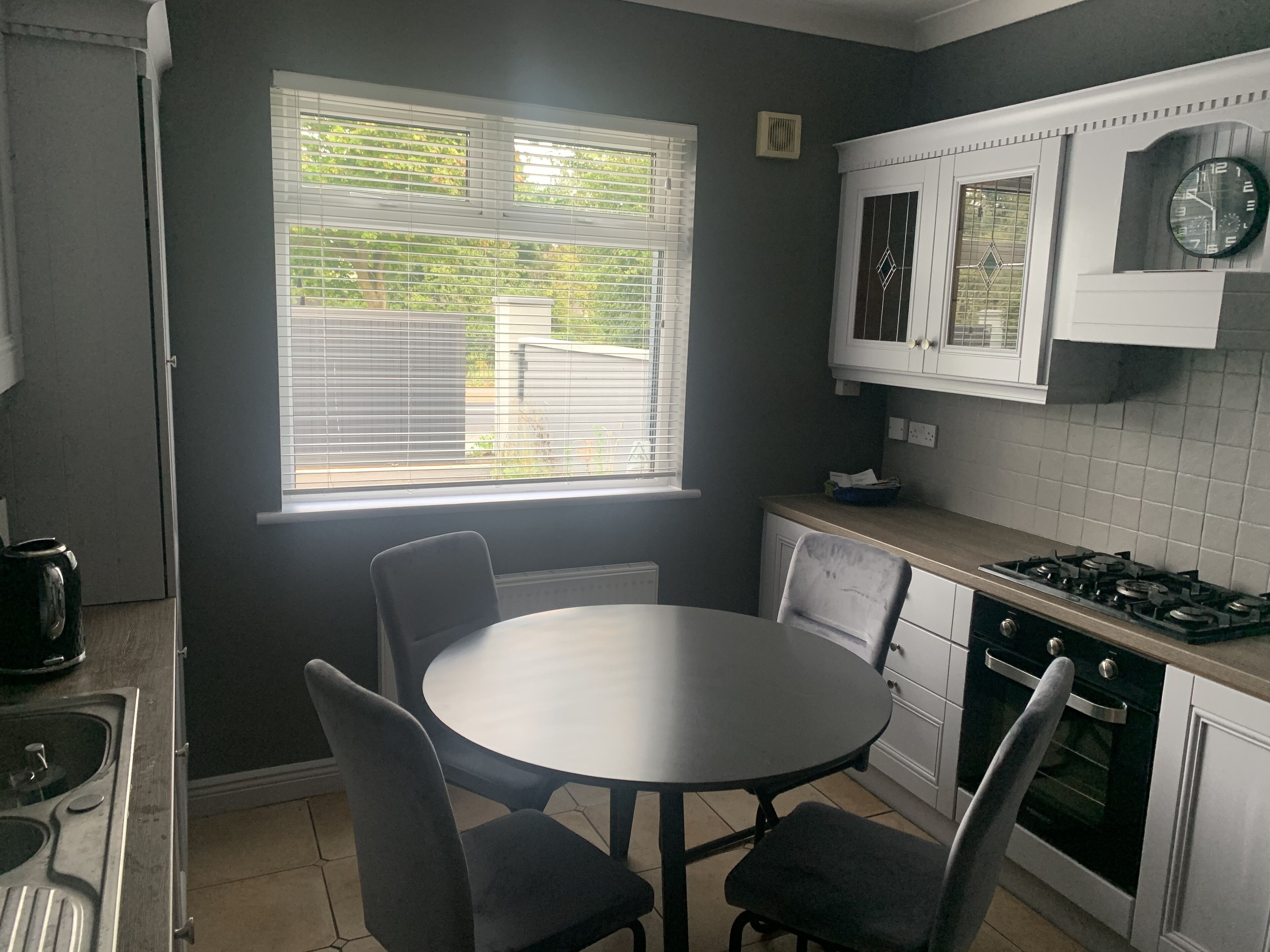 A kitchen with a round table and chairs, a stove, cabinets, and a window with blinds.