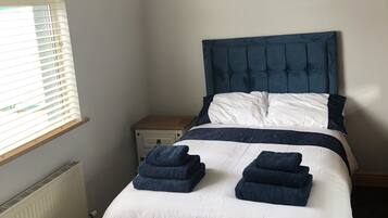 A bedroom with a bed, a bedside table, a radiator, and a window with blinds.