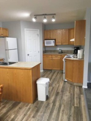 Una cocina compacta con armarios de madera, un refrigerador, un microondas y un lavamanos.