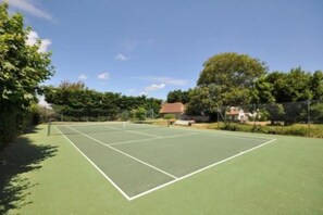 An outdoor tennis court with a net, surrounded by trees and a house in the background.