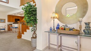 A spacious living area with a staircase, a dining set, and a glass console table with decorative items. - Luxury Villa • AC • Golf Views • Walk to Pool, Beach & Shop (Waikoloa)