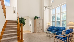 A spacious living room with a staircase, a blue sofa set, a wooden rocking chair, and a glass coffee table. - Luxury Villa • AC • Golf Views • Walk to Pool, Beach & Shop (Waikoloa)