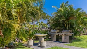 An outdoor patio with a stone table and two barbecue grills. - Luxury Villa • AC • Golf Views • Walk to Pool, Beach & Shop (Waikoloa)
