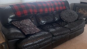 A black leather sofa with a red and black checkered throw blanket, a woven pillow, and a ruffled pillow. - Family Friendly Cardston  (whole house)! (Cardston)