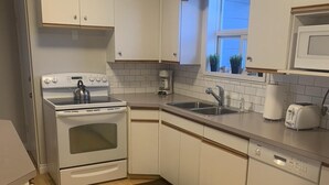 A compact kitchen with white cabinets, a built-in oven, a sink, and a dishwasher. - Family Friendly Cardston  (whole house)! (Cardston)