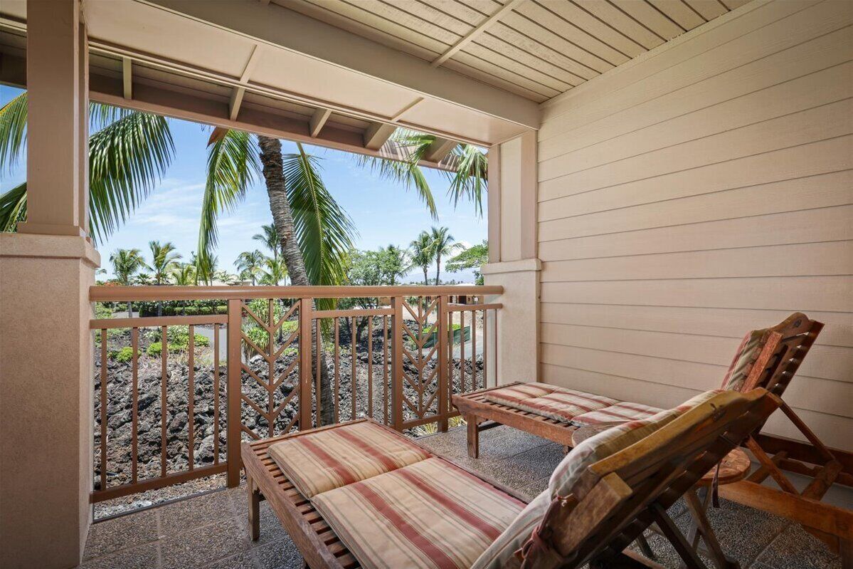 A covered outdoor seating area with a view of palm trees and a rocky landscape.