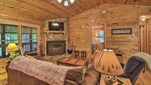 A cozy cabin interior with a stone fireplace, wooden walls, a ceiling fan, and a television mounted on the wall. - 'Pinot & Pine' Chic Log Cabin ~ 5 Mi to Blue Ridge (Blue Ridge)