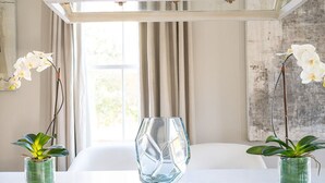 A dining area with a white table, two chairs, a hexagonal glass vase, and two potted plants. - Explore Magazine Street from a Chic, Tranquil Home (New Orleans)