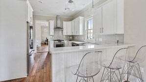 A modern kitchen with white cabinetry, a central island, and bar stools. - Explore Magazine Street from a Chic, Tranquil Home (New Orleans)