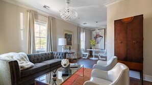 A modern living room with a dark grey sofa, white armchairs, a glass coffee table, and a wooden cabinet. - Explore Magazine Street from a Chic, Tranquil Home (New Orleans)