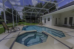 Une piscine extérieure couverte, dotée d’un jacuzzi, entourée d’une maison blanche et d’une pelouse.