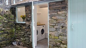 A laundry room with a washing machine, a window with a flower vase, and a stone wall. - 4 bedroom accommodation in Ambleside (Ambleside)