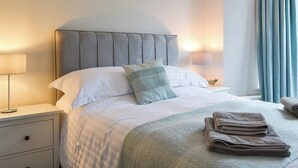 A neatly made bed with a grey upholstered headboard, white linens, and a folded towel on the bed. There are two bedside lamps on either side of the bed, and a small decorative item on the nightstand. - 4 bedroom accommodation in Ambleside (Ambleside)