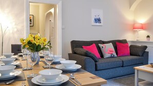 A dining area with a table set for four, a grey sofa with pink cushions, and a wall-mounted lamp. - 4 bedroom accommodation in Ambleside (Ambleside)