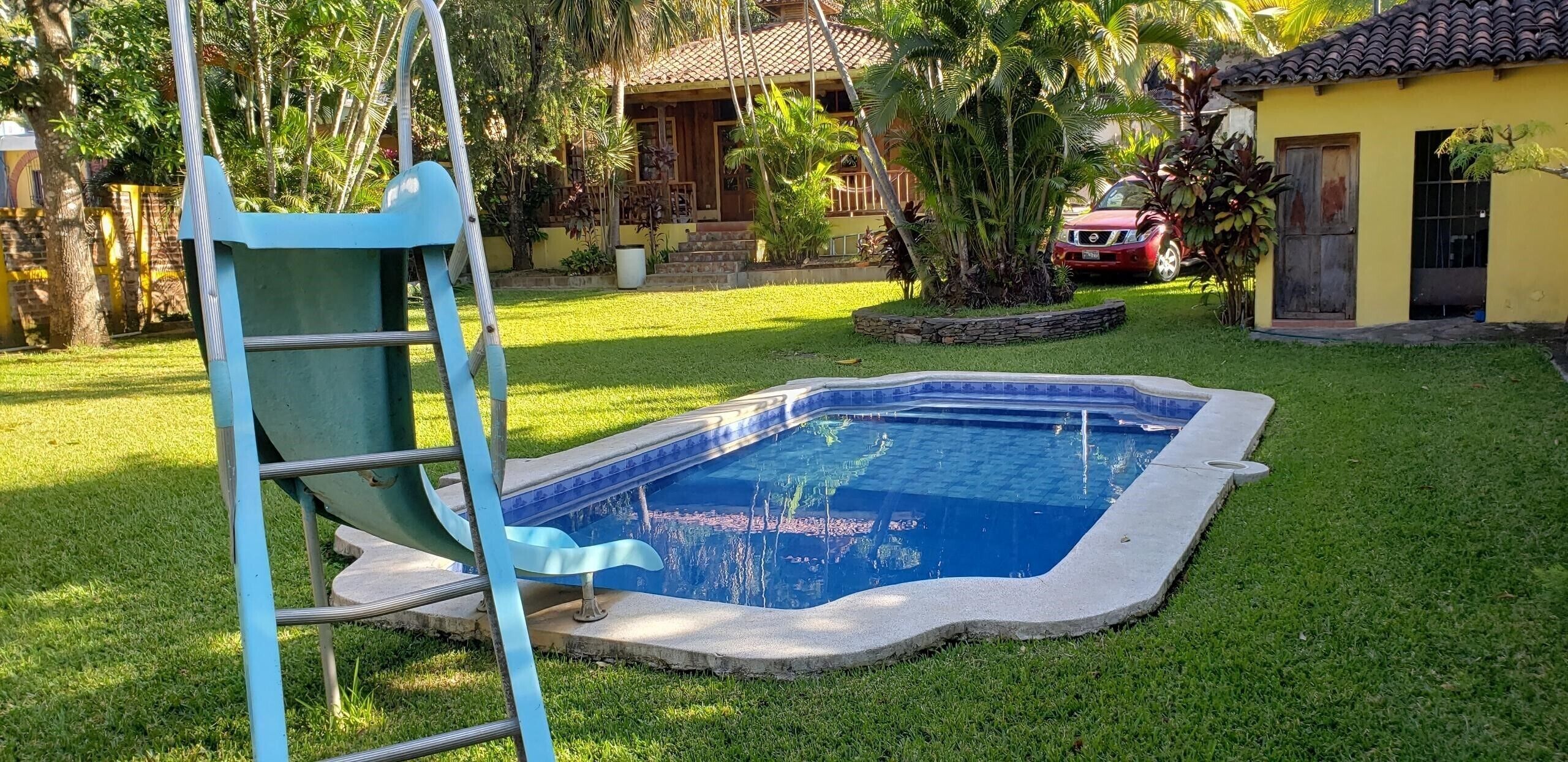 Una piscina con borde azul, rodeada por un césped bien cuidado y una escalera pequeña de color azul.