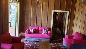 A room with a wooden paneled wall, a pink sofa with patterned cushions, and two red armchairs.