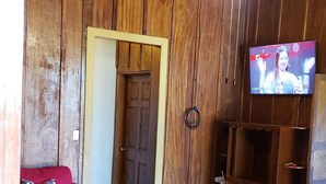 A wooden-paneled room with a television, a red sofa, a wooden coffee table, and a tiled floor.