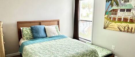 A bedroom with a bed, a ceiling fan, a window with curtains, and a wall painting.