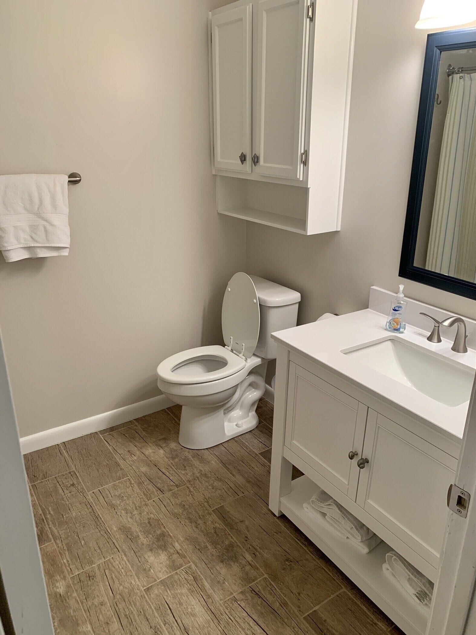 A bathroom with a toilet, sink, mirror, and cabinets.