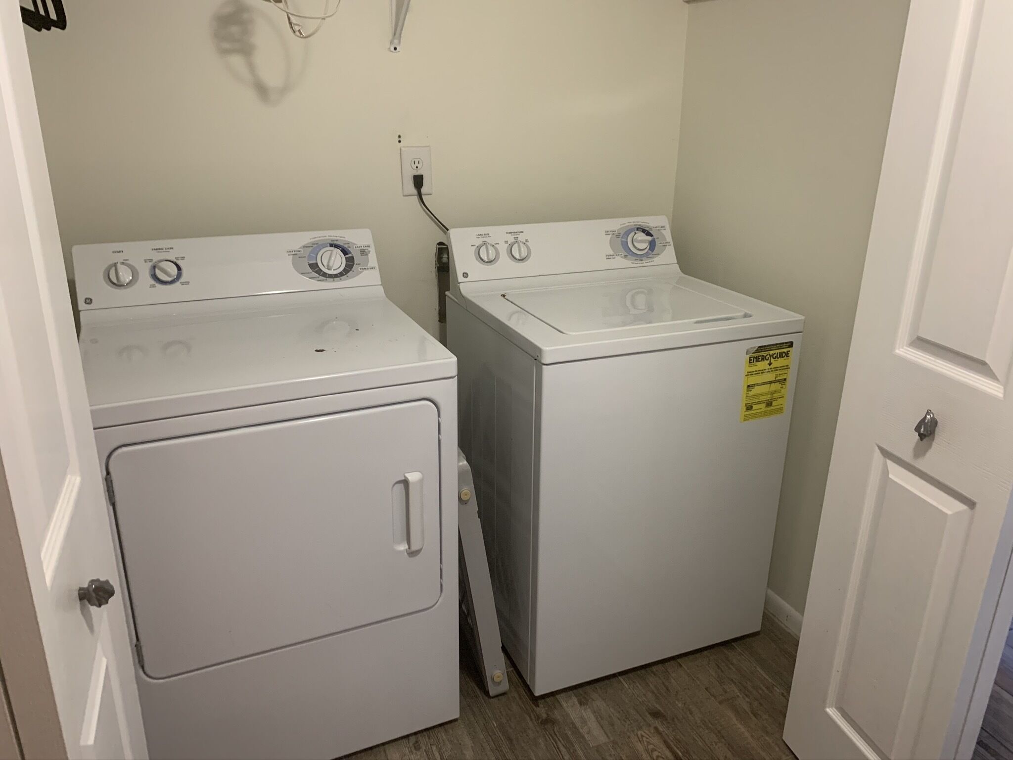 A laundry room with two stacked washers and dryers, a power outlet, and a door.