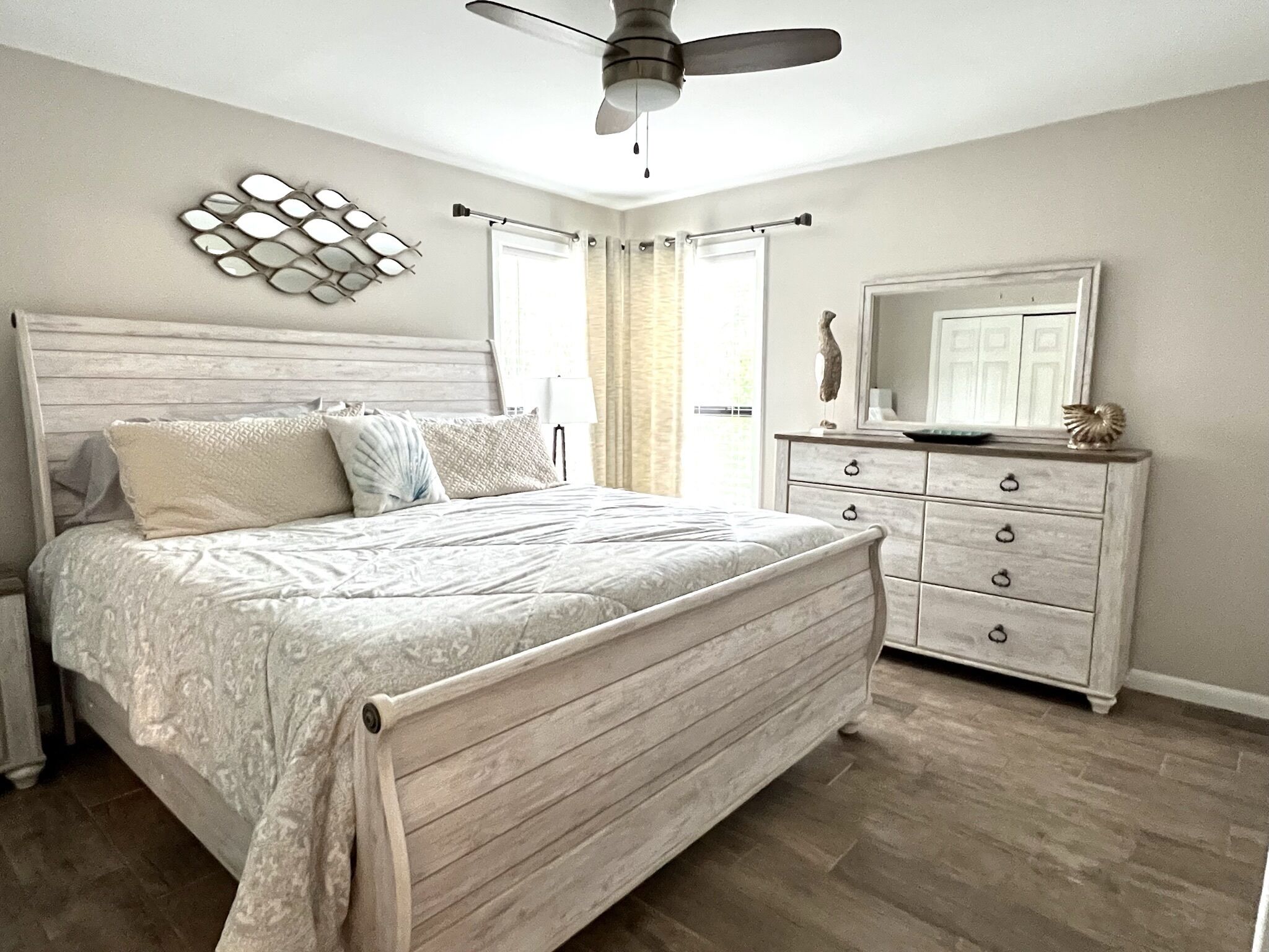 A bedroom with a wooden bed, a dresser, a ceiling fan, and a decorative wall piece.