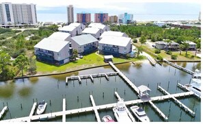 A marina with several boats docked, surrounded by modern buildings with flat roofs and a grassy area in the foreground.