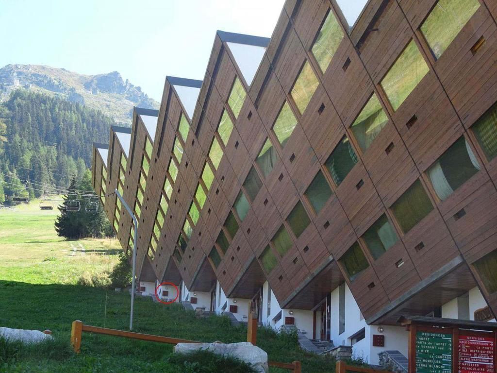 Una hilera de cabañas de madera con un diseño único de techo en forma de rombo, frente a un telón de fondo montañoso.