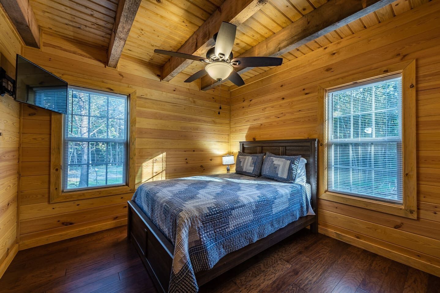Ein Schlafzimmer einer Holzhütte mit Bett, Deckenventilator und großen Fenstern.