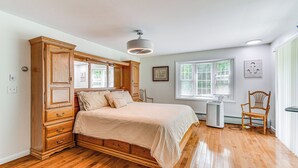 Une chambre avec un lit en bois, un ventilateur de plafond, une fenêtre et une chaise.