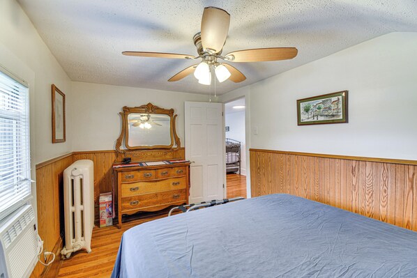 A bedroom with a bed, a ceiling fan, a dresser, a mirror, and a radiator.