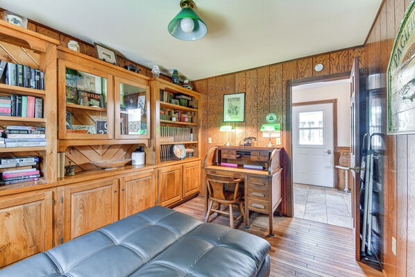 A cozy room with a wooden bookshelf, a desk, a leather bench, and a refrigerator.