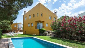 Un bâtiment jaune avec une piscine, entouré de verdure et agrémenté d’un arbuste à fleurs roses.