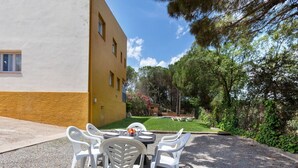 Une terrasse avec une table et des chaises, une piscine et un bâtiment à la façade jaune.