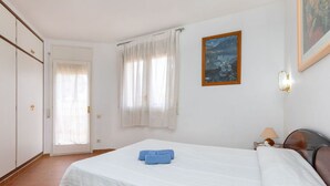 Une chambre à coucher avec un lit, une table de chevet, une lampe, un tableau et une porte.