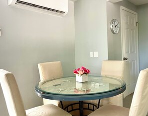 A round glass table with beige chairs, a vase of pink flowers, and a clock on the wall. - House 2 min walk to Grace Bay Beach - 2b/1b, for 4, pool, AC, WiFi (The Bight Settlement)