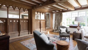 Quarto tradicional com vigas de madeira, um guarda-roupa espaçoso, um sofá e uma janela com cortinas.
