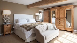 Quarto com uma cama grande, um guarda-roupa de madeira, uma poltrona branca e duas mesas de cabeceira com luminárias.