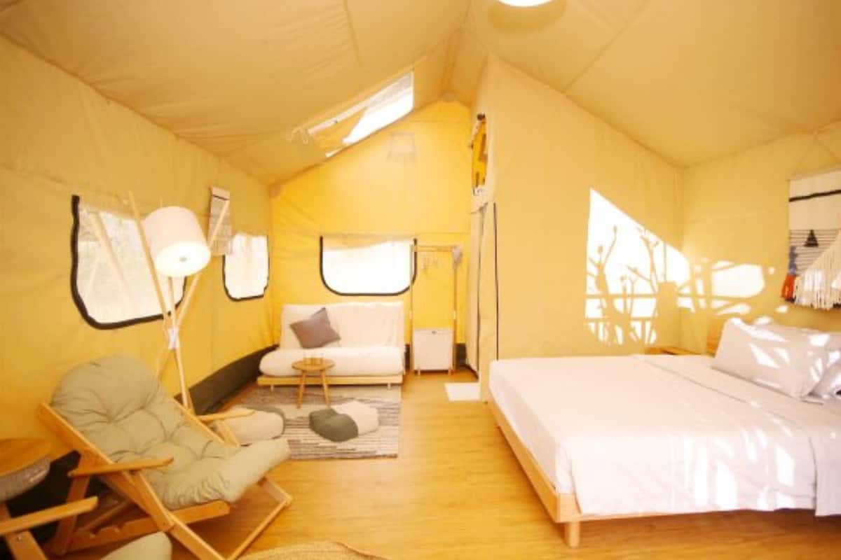Une pièce compacte et bien éclairée, comprenant un lit, un coin salon avec un fauteuil et une petite table.