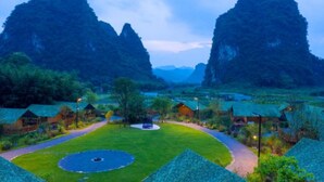 Un resort con un césped central, senderos y cabañas rústicas rodeadas de terreno montañoso.