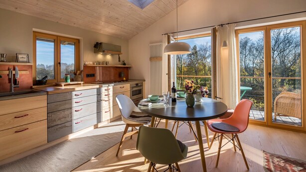 Una cocina moderna con armarios de madera, un comedor con mesa redonda y amplias ventanas que ofrecen vistas al exterior.